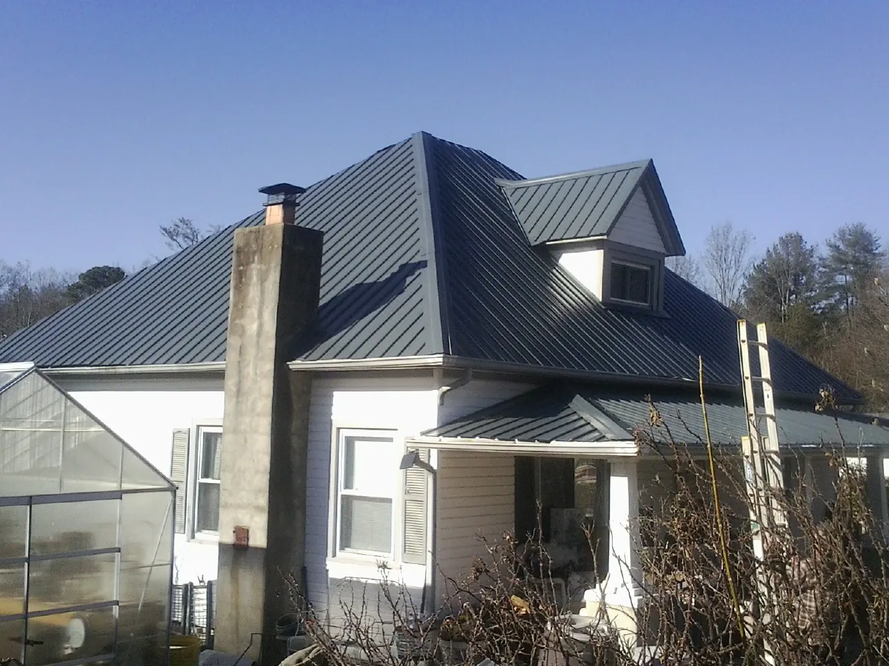 Dark blue standing seam metal roof on a white farmhouse with dormer — Slate & Tile Roof Repair by Roofing Brothers in Locust Fork