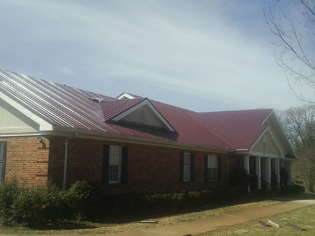 Red metal roof with gabled entries on a long brick building, from a Hail Damage Roof Repair job in Locust Fork