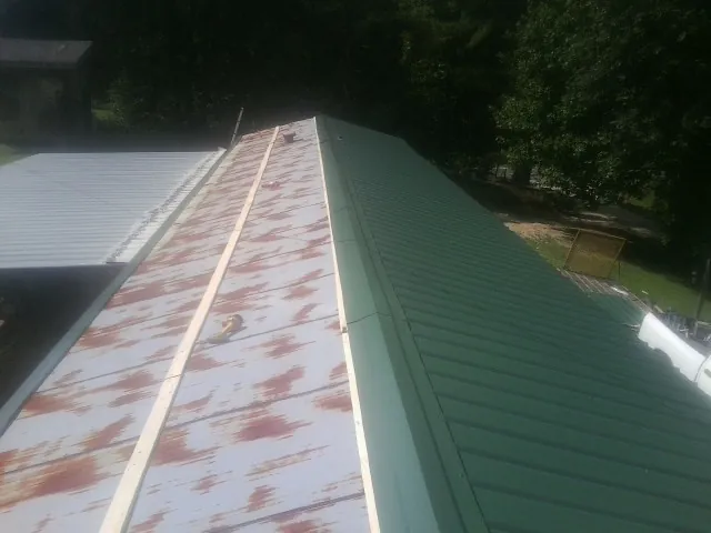 Old rusted panels beside newly installed green metal roofing — Wind Damage Roof Repair by Roofing Brothers in Locust Fork