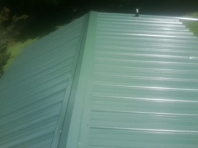 New green metal panels meeting at the ridge of a roof — Flat Roof Repair work by our crew in Locust Fork