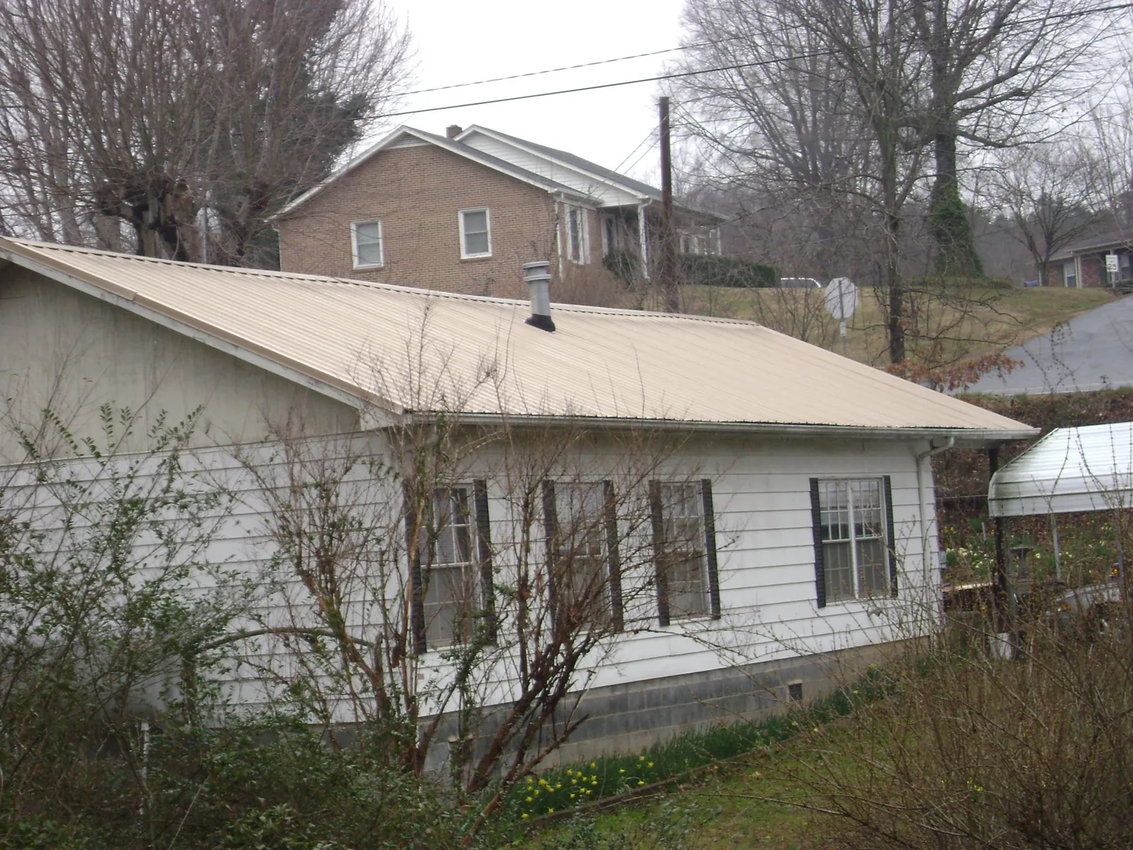Tan metal roof on a white sided house set into a hillside — Commercial Roofing by Roofing Brothers in Locust Fork