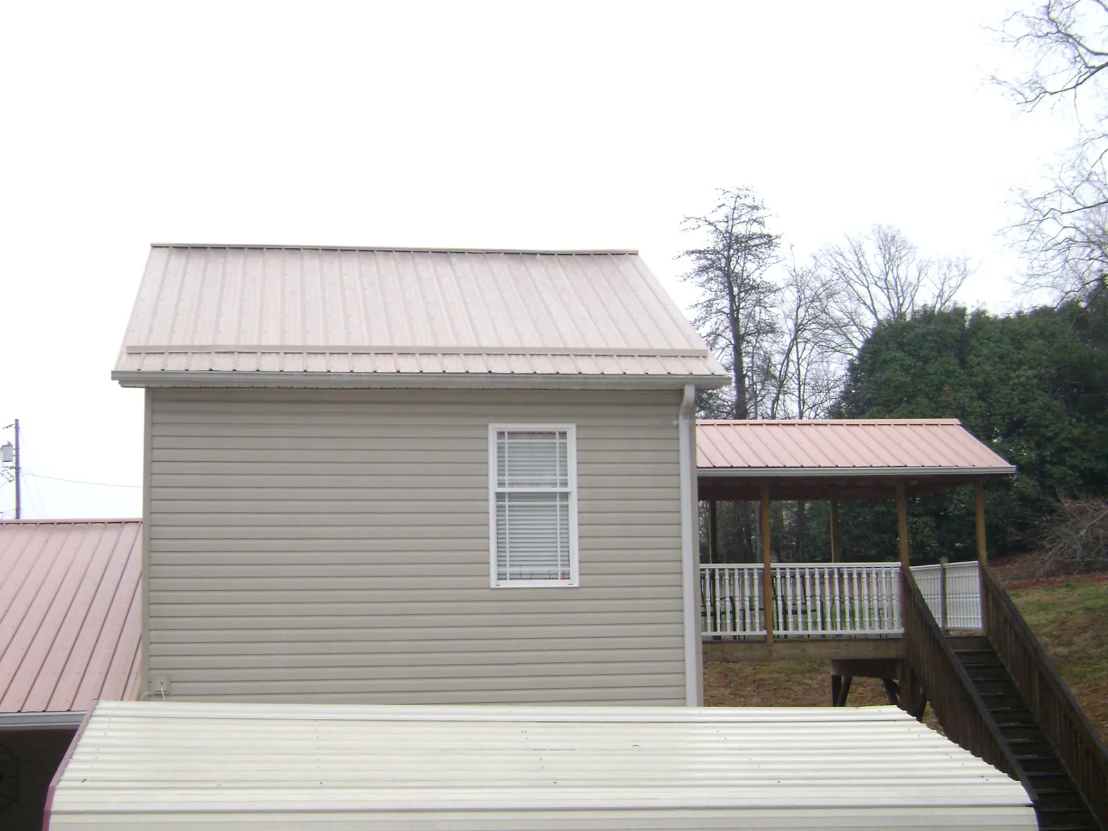 Tan metal roofs on a two story addition and attached porch, from a Roof Replacement job in Locust Fork